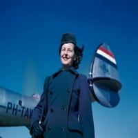 Smiliranje člana ženskog kabinskog posade koji stoji u blizini aviona protiv plavog nebaskog plakata